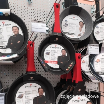 Metalowe haki sklepowe na ścianie perforowanej z zawieszonymi patelniami – zdjęcie poglądowe, widok pod kątem